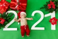 A 6 month old baby in a Santa costume lies on a green background with the inscription 2021 and gifts