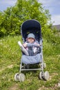 A 9 month old girl sits in a summer carriage and plays with her legs. Little smiling child in a hat on a walk, summer day