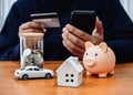 Monthly expenses, budget, financial insurance concepts. White home, car, money coin bottle and piggy bank on table while person Royalty Free Stock Photo