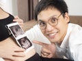 3 months Pregnant Asian couple in white bed room looking at 3d ultrasound x-ray film. A man touching woman`s abdomen. Royalty Free Stock Photo