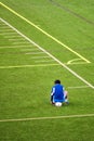 Unhappy teenage boy excluded from the soccer team sits on the ball at the corner of the green football field