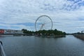 Montreal Grand Ferris Wheel in Old Port. Background is a blue cloudy sky. Foreground is trees and Saint Laurent River