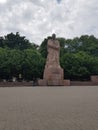 Monument of Ivan Frank from the brown stone, in the square under the open sky, which is covered with dark clouds. Behind the monu