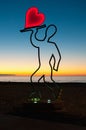 Monument Love on the embankment at sunset. Silhouette of a man with a glowing red heart