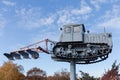 Monument to old caterpillar tractor with mounted plough against sky