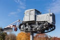 Monument to old caterpillar tractor with mounted plough against sky