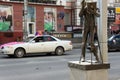 Monument to the photographer against the background of wedding cars on a city street.