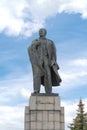 Monument to Ulyanov Lenin against a blue clear sky with white clouds next to beautiful fir trees with cones