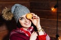 The mood of winter. Young beautiful dark-haired woman smiling in clothes and cap with tangerines on wooden background.