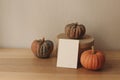 Moody autumn still life, Blank greeting card invitation mockup with orange pumpkins, gift box on wooden table. Halloween