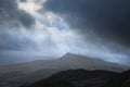 Moody and dramatic Winter landscape image of Moel Saibod from Crimpiau in Snowdonia with stunning shafts of light in stormy