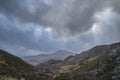 Moody and dramatic Winter landscape image of Moel Saibod from Crimpiau in Snowdonia with stunning shafts of light in stormy