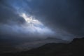 Moody and dramatic Winter landscape image of Moel Saibod from Crimpiau in Snowdonia with stunning shafts of light in stormy