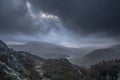 Moody and dramatic Winter landscape image of Moel Saibod from Crimpiau in Snowdonia with stunning shafts of light in stormy