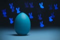 Moody easter concept in classic blue color. Blue cyan colored egg on black background with bunny shaped bokeh. Selective focus.