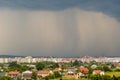 Moody landscape with dark stormy clouds with falling heavy downpour shower rain over distant town buildings in summer Royalty Free Stock Photo