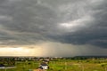 Moody landscape with dark stormy clouds with falling heavy downpour shower rain over distant town buildings in summer Royalty Free Stock Photo