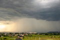 Moody landscape with dark stormy clouds with falling heavy downpour shower rain over distant town buildings in summer Royalty Free Stock Photo