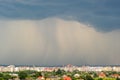 Moody landscape with dark stormy clouds with falling heavy downpour shower rain over distant town buildings in summer Royalty Free Stock Photo