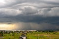 Moody landscape with dark stormy clouds with falling heavy downpour shower rain over distant town buildings in summer