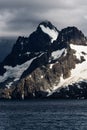 Moody mountain scene highlighted by a sunbeam, with stormy clouds, blue ocean, and snow and glacier on the island mountain, Drygal Royalty Free Stock Photo