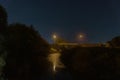 A moody night scene of street lights reflected in a river. With a bridge in the background