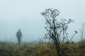 A moody out of focus hooded ghostly figure standing in the background on a foggy winters day. With a muted edit