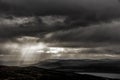 Moody woodland and lake landscape with sun beams through clouds