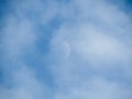 Moon during day in the blue sky between clouds.