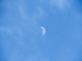 Moon during day in the blue sky between clouds.