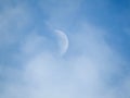 Moon during day in the blue sky between clouds.