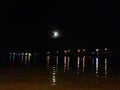 Moon peaking out from behind clouds reflecting over water