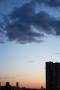 The moon is peeking out from behind the dark evening clouds over the roof of city houses.