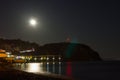 The moon reflects in the water on the beach.