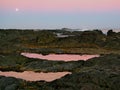 Full moon rising over rockpools, with pink sunset reflecting in the water. Royalty Free Stock Photo