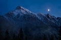 Moon rising over a snowy mountain range on a foggy evening Royalty Free Stock Photo