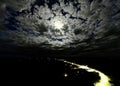 the moon sets above a cloudy night sky near a river