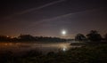 Moon shining in the sky full of stars and reflected in the lake below Royalty Free Stock Photo