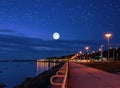 Moon on starry sky in harbor ,blurred city light at night ,pink sunset at sea ,ship on horizon seafront people walk promenade b