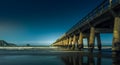 The moonlit Historic wharf at Tolaga Bay in the dark with gentle surf waves rolling in