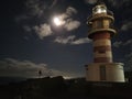 Moonlit path on the ocean and a beautiful large lighthouse on the rocky coast. Night lighthouse