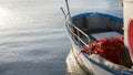 The moored fishing boat is lulled by the water while the sun reflects on the sea early in the morning with the red fishing net in