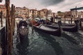 Moored gondolas around a wooden pier and buildings on the bank of Grand Canal in a rainy autumn day, Venice, Italy