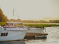 Moored pleasure boat and motorboat near the old wooden pier on the lake in the evening with sunset light on the background Royalty Free Stock Photo