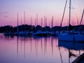 Moored sailing yachts on a jetty with reflection in the water at beautiful pink dusk