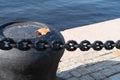 Mooring bollard on a background of blue water surface, loaf embankment, cast-iron chain