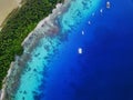 Aerial view of five yachts moored inside a vibrant tropical atoll behind an island in pristine, clear water.