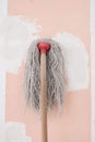 the mop with long cotton gray threads on wooden the stick on the background of the wall pink color with white spots during repair