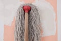 the mop with long cotton gray threads on wooden the stick on the background of the wall pink color with white spots during repair