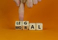 Moral or legal symbol. Businessman hand turns wooden cubes and changes the word `moral` to `legal` on a beautiful orange table
